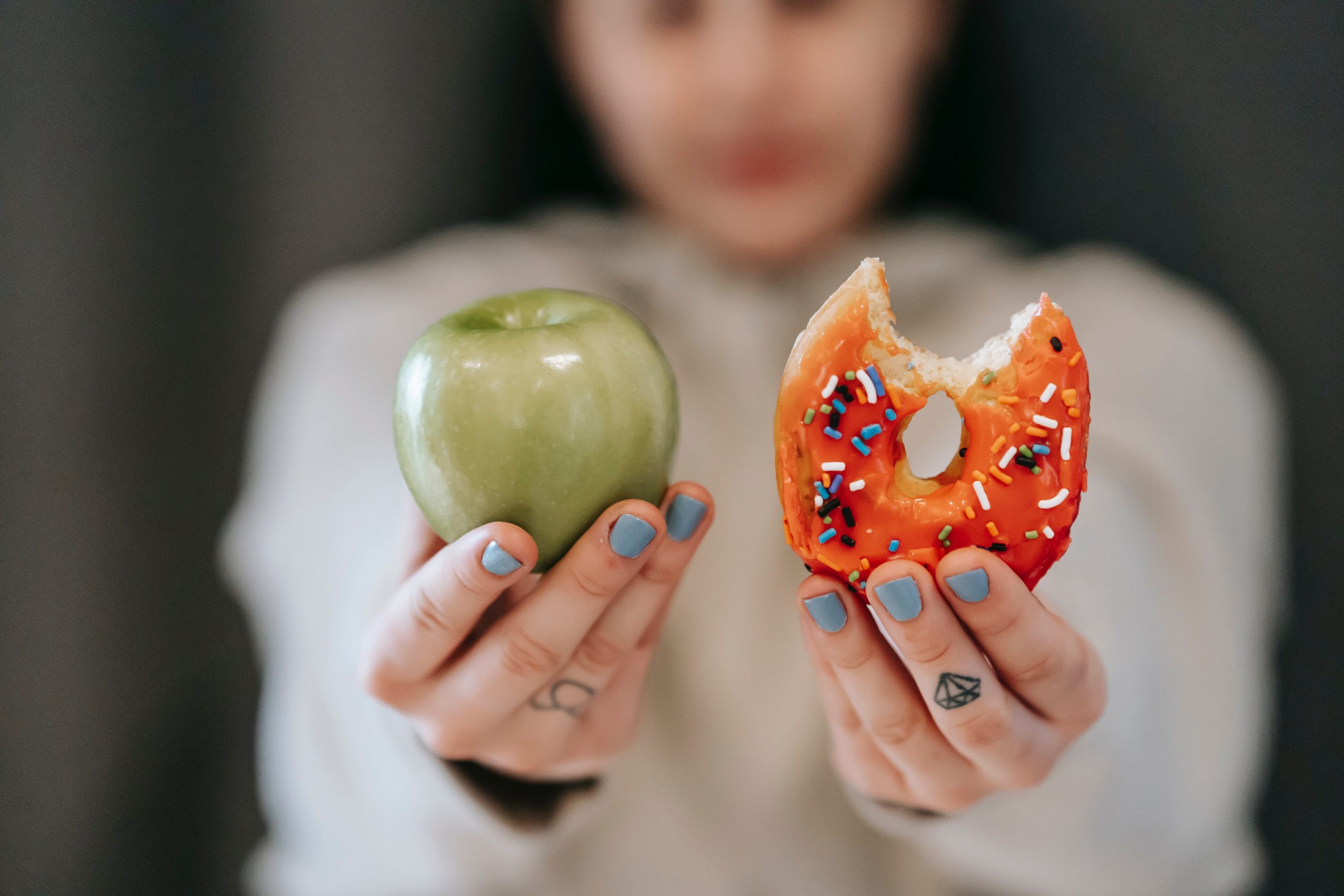 Woman holding a bitten donut in one hand and an apple in the other.