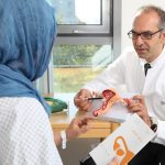 Prof. Dr. med. Dr. h.c. Jalid Sehouli, Charité Berlin, speaks to a patient with a headscarf using a model of ovaries.